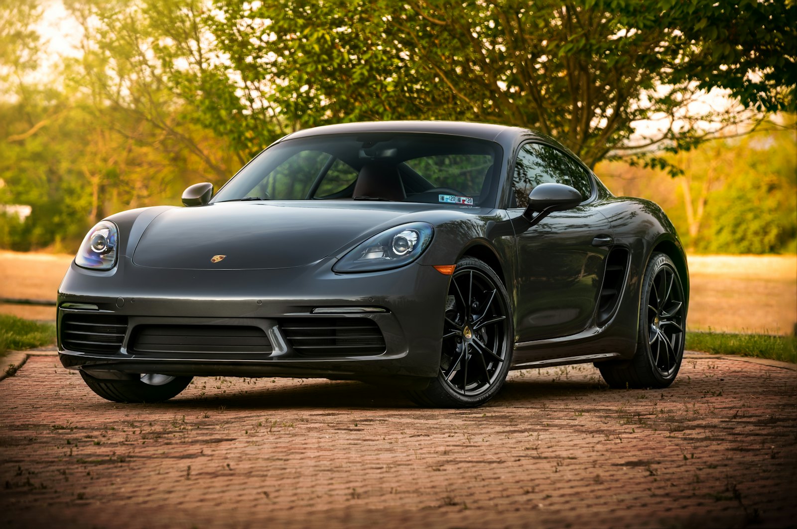 A dark grey Porsche coupe parked on a brick driveway